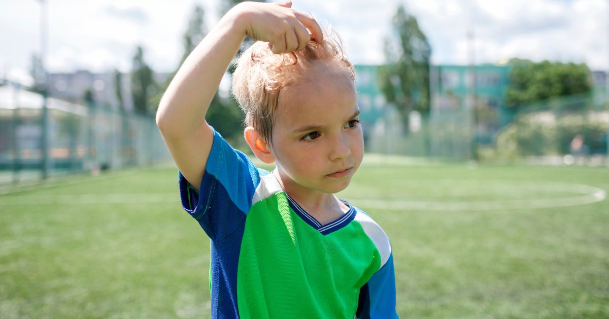 A boy playing outside pushes his sweaty hair off of his forehead.