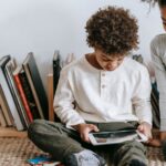 A brother and sister sit on the floor while looking at a tablet.
