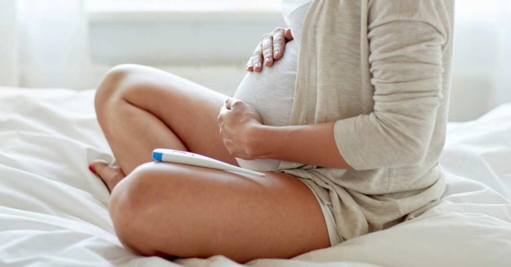 A close up of a pregnant woman's belly with a thermometer nearby.