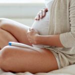 A close up of a pregnant woman's belly with a thermometer nearby.