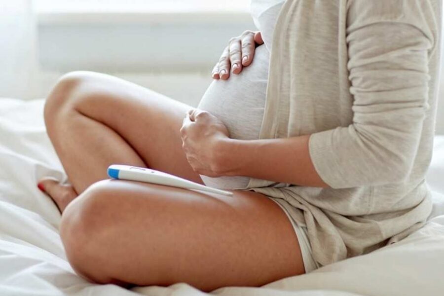 A close up of a pregnant woman's belly with a thermometer nearby.