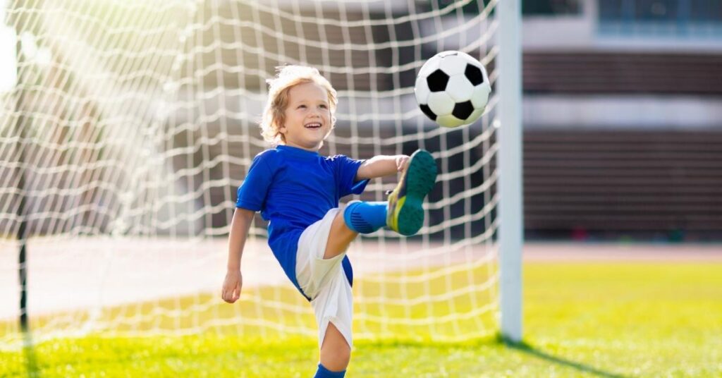 A boy kicks a soccer ball in front of a goal.