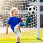 A boy kicks a soccer ball in front of a goal.