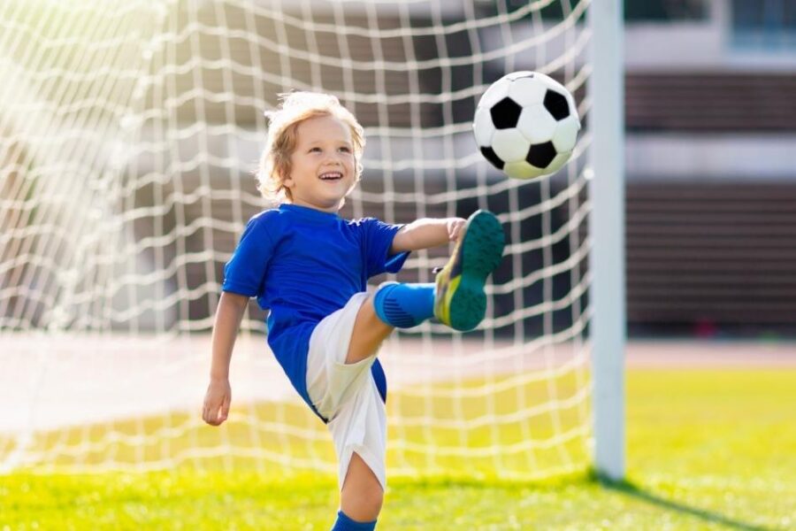 A boy kicks a soccer ball in front of a goal.