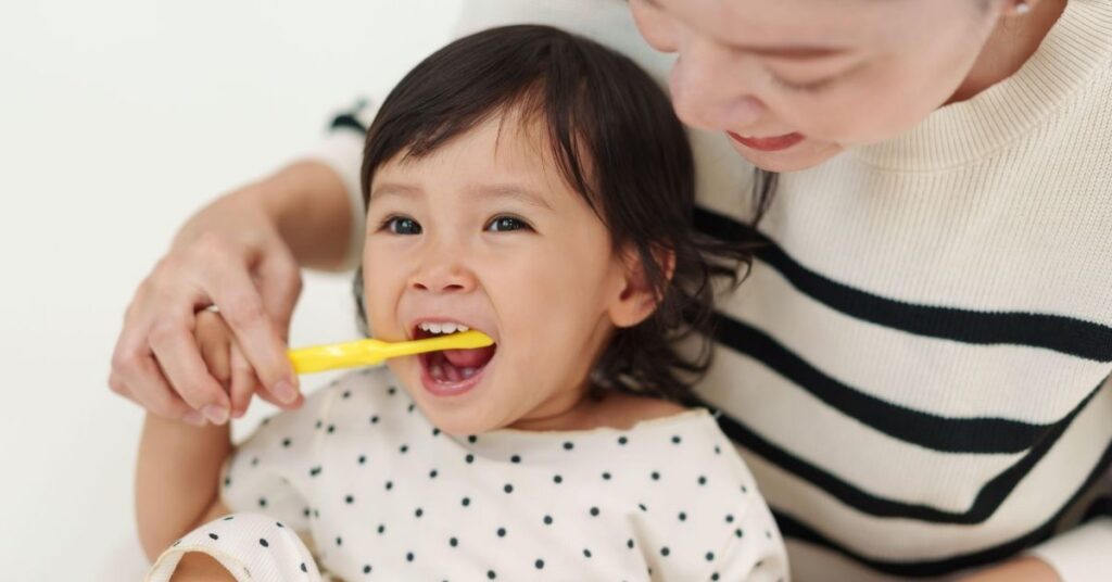 A mom helps brush her toddler's teeth.