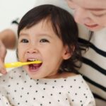 A mom helps brush her toddler's teeth.
