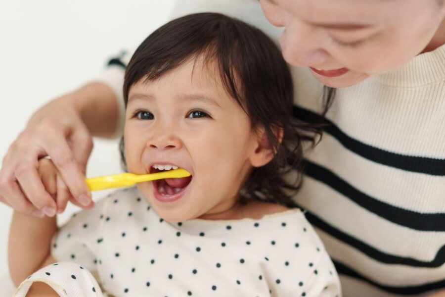A mom helps brush her toddler's teeth.